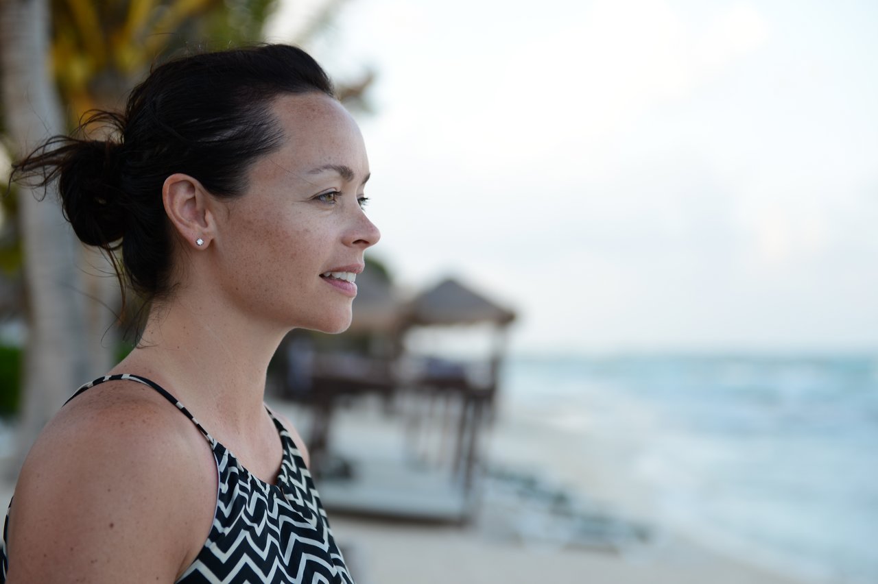 A woman stands on a beach, looking into the distance with a calm expression.