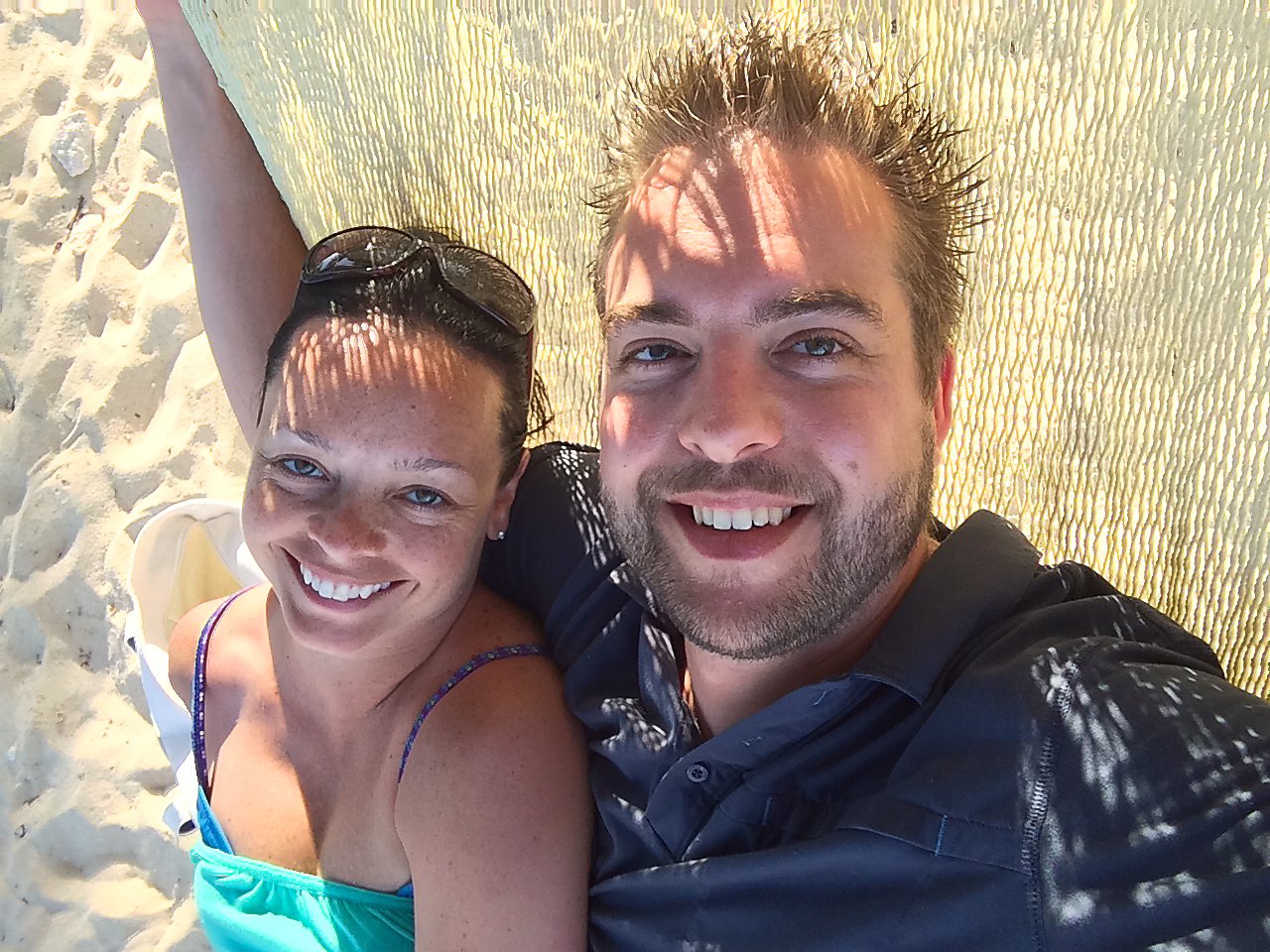 A smiling couple relaxes together in a hammock on a sandy beach in Cancun.