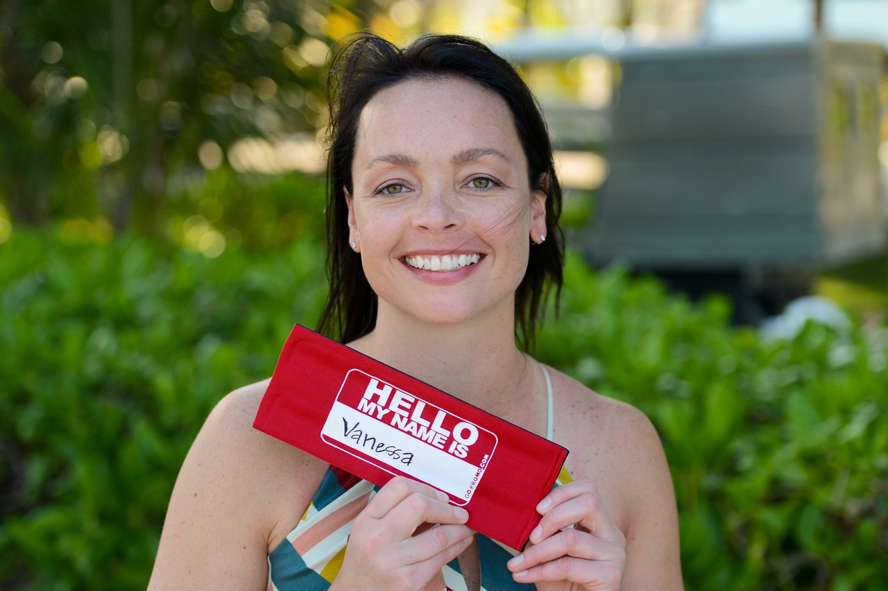 A woman smiles while holding a red name tag that says "Hello, my name is Vanessa.