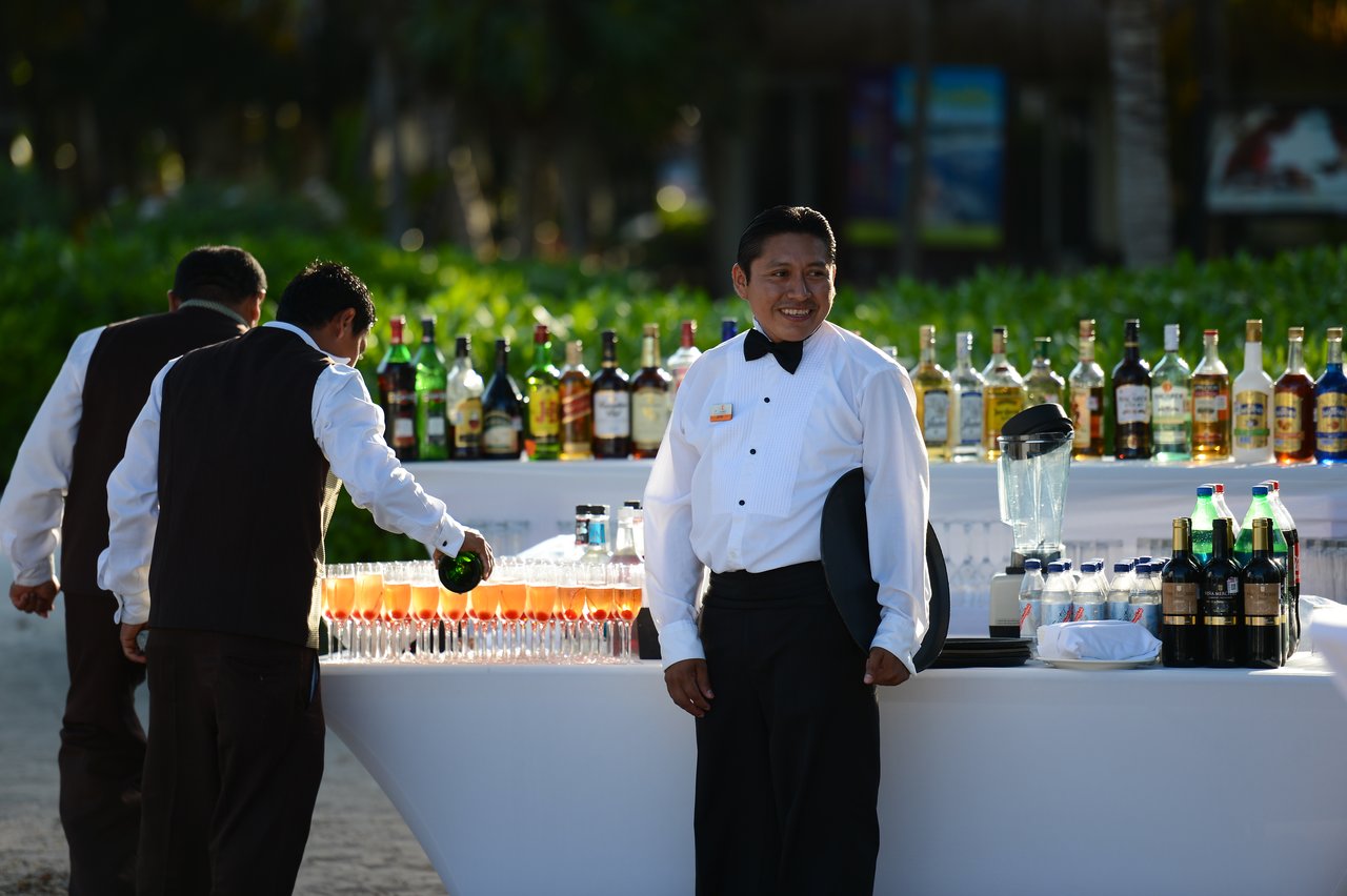 Bartenders in formal attire prepare and serve drinks at an outdoor bar with bottles and glasses neatly arranged.