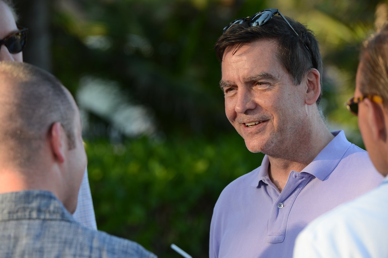 A man in a purple shirt smiles while talking with three other people outdoors.