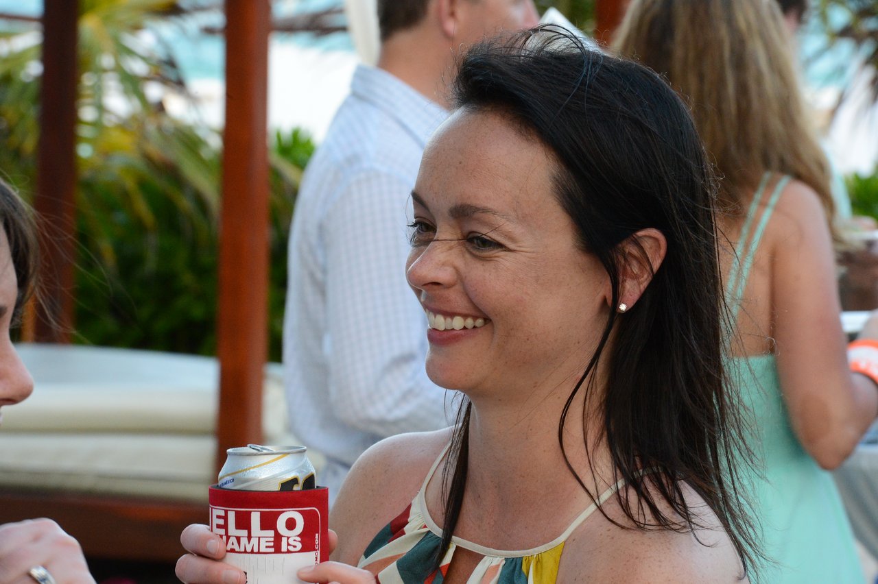A smiling woman holds a drink and talks with another person at an outdoor gathering in Cancun.
