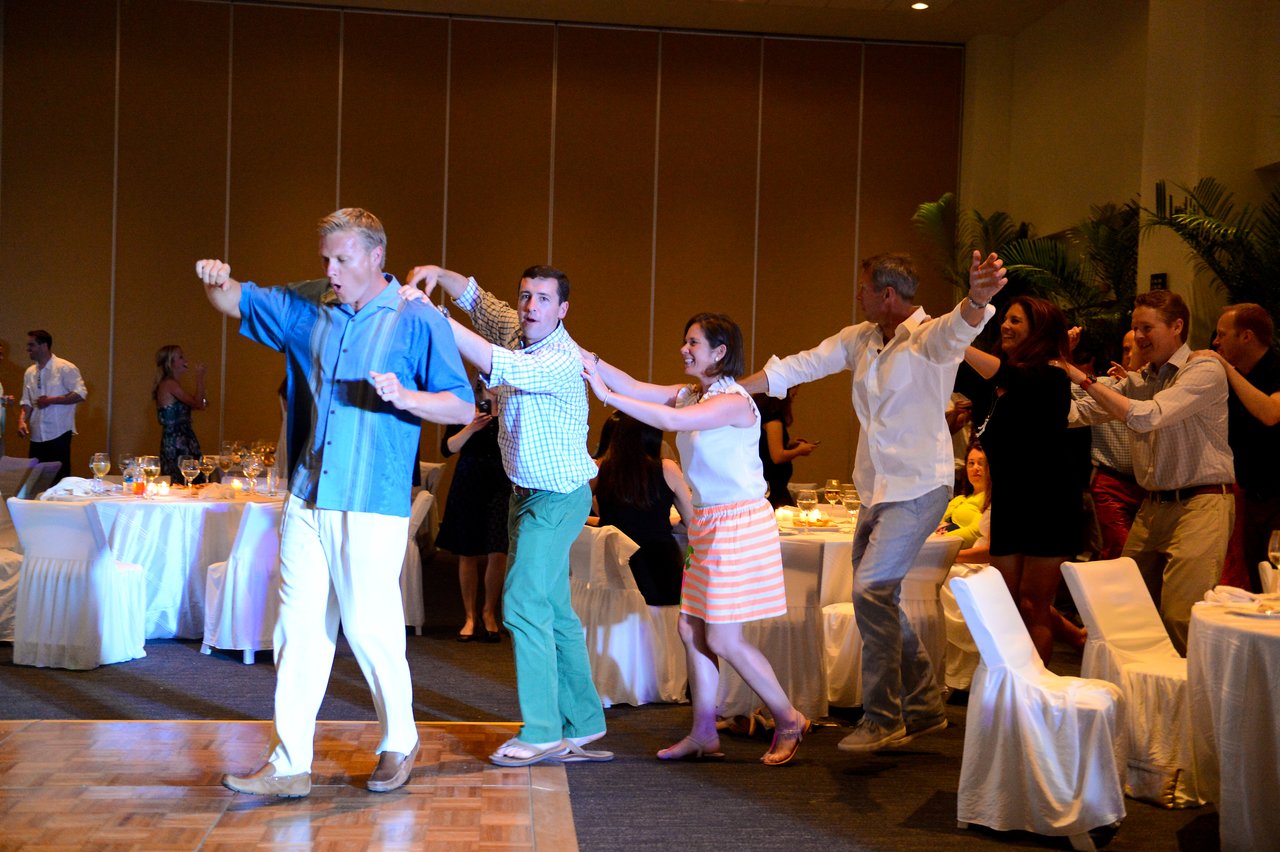 A group of people dances in a conga line at an indoor event, smiling and having fun.