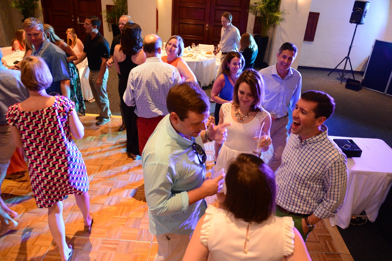 A group of people socializing and laughing at an indoor event, holding drinks and engaging in conversation.