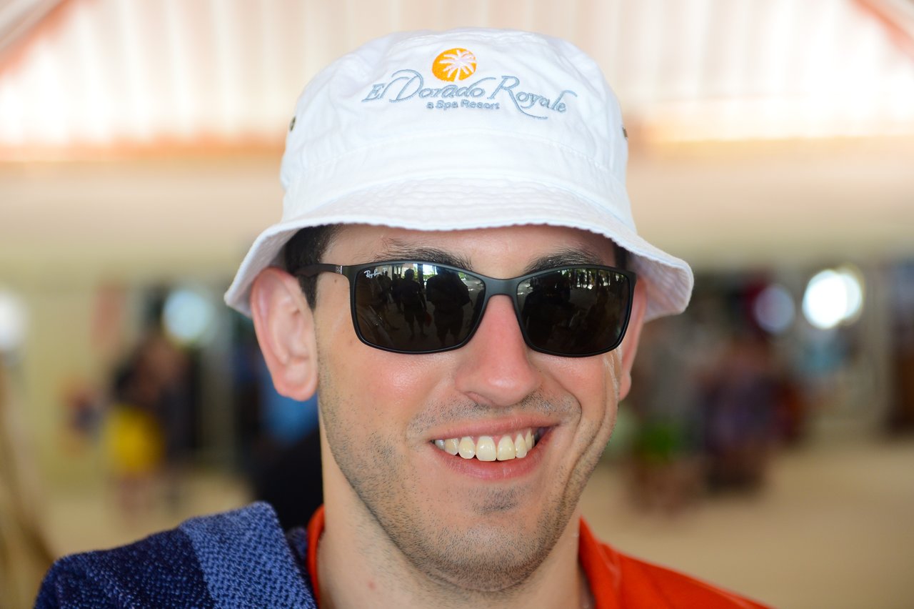 A man wearing sunglasses and a white bucket hat smiles at the camera.