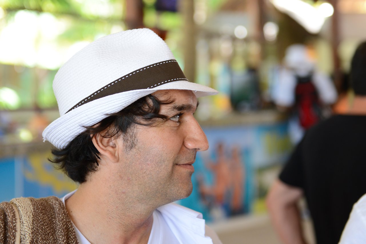 A man wearing a white hat looks to the side in a busy indoor setting.