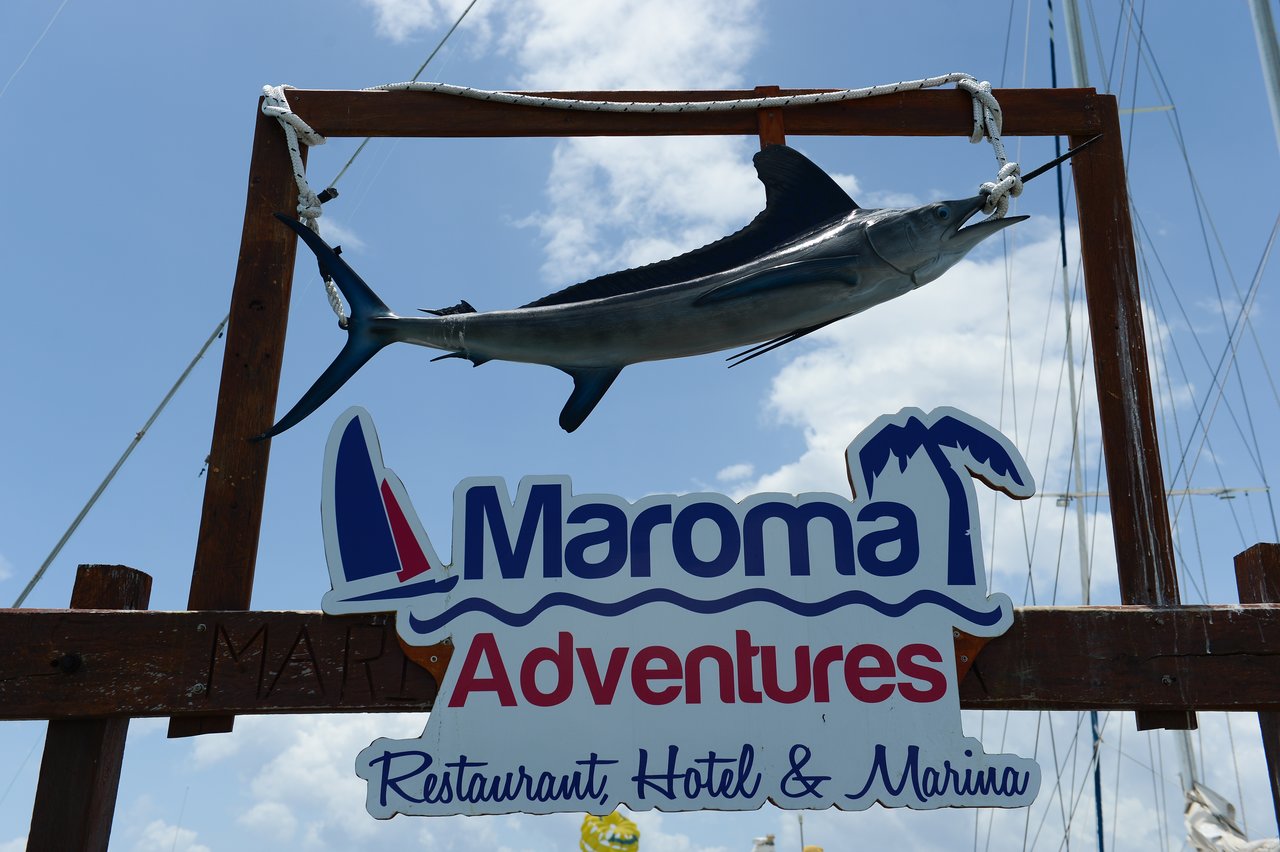 A wooden sign for "Maroma Adventures" with a mounted fish above it, advertising a restaurant, hotel, and marina.