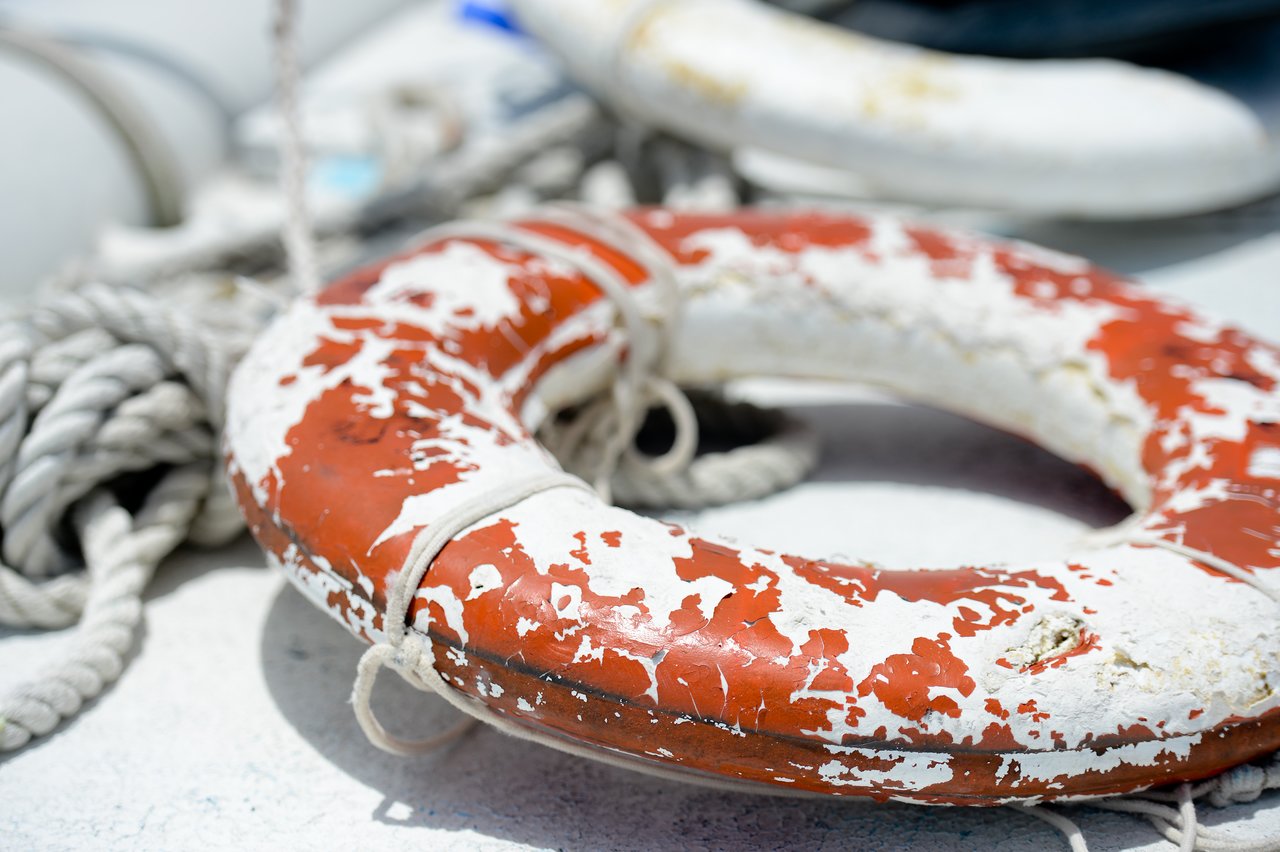 A weathered orange and white lifebuoy with ropes rests on a boat deck in Cancun.