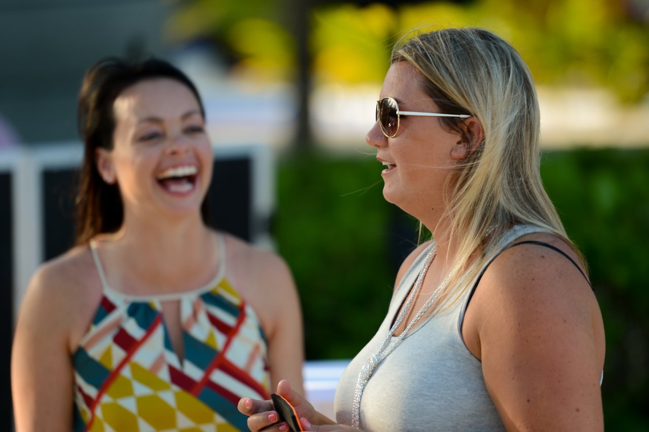 Two women standing outdoors, one laughing while the other speaks and holds a phone.
