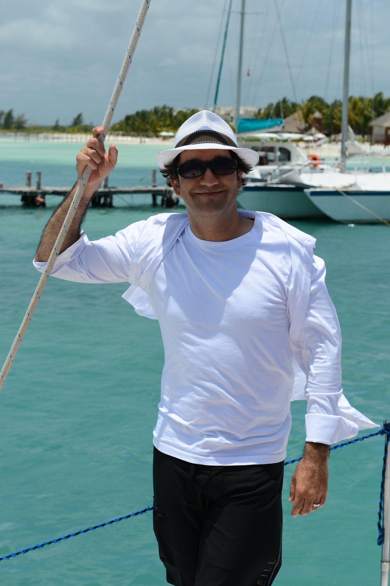 A man in a white shirt and hat smiles while holding a rope on a boat in Cancun.