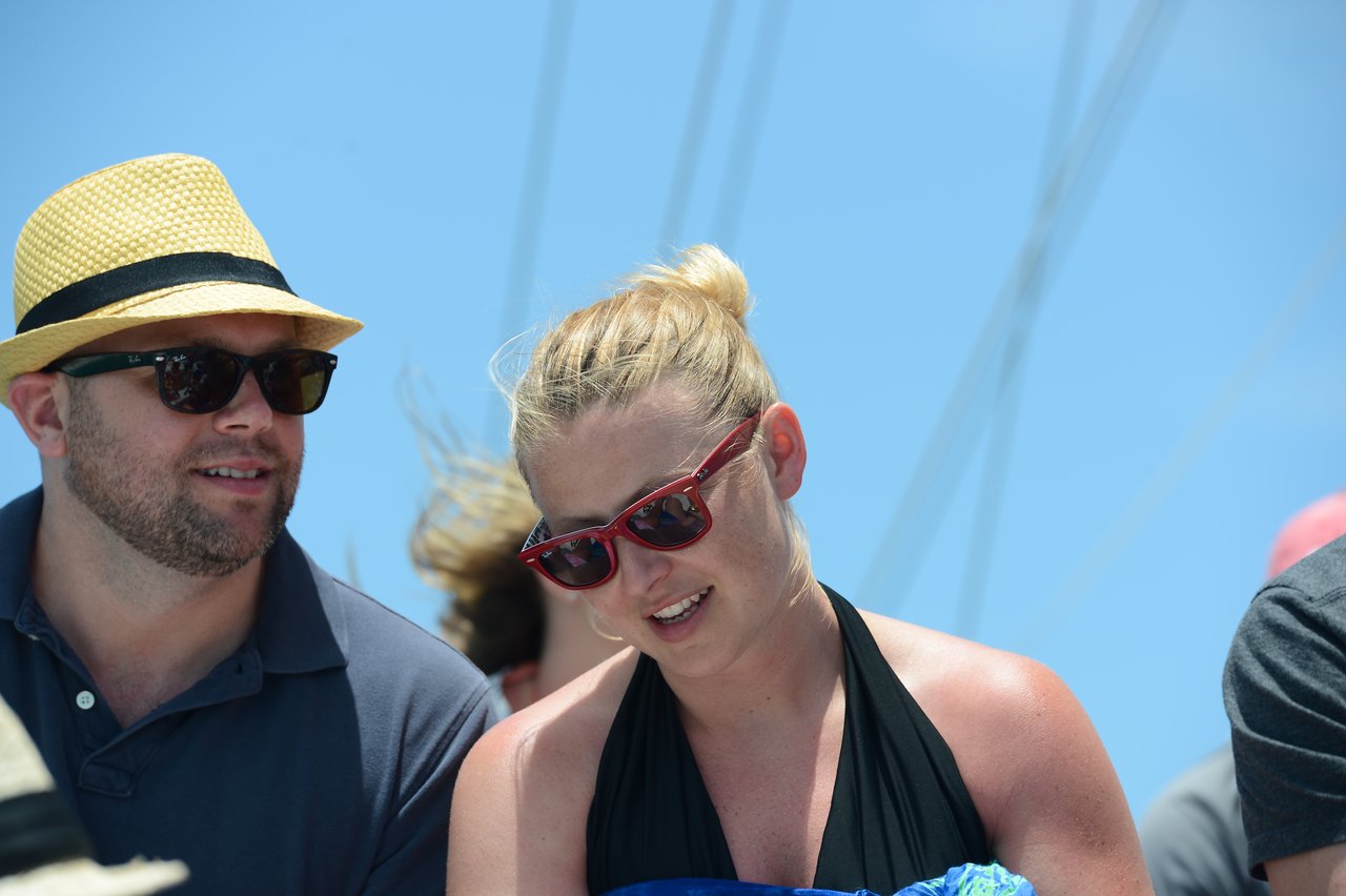 A man and a woman wearing sunglasses sit together outdoors under a bright sky, engaged in conversation.