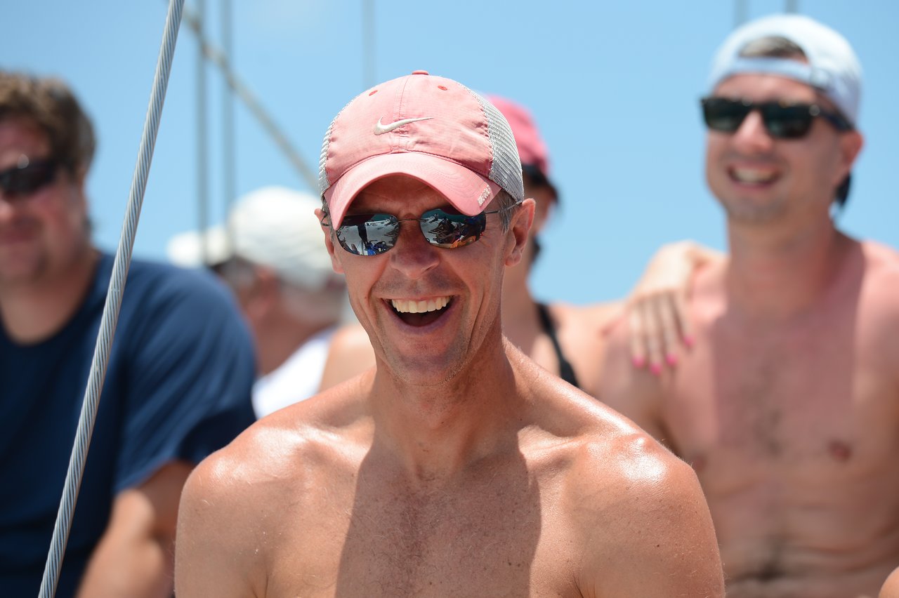 A smiling man in sunglasses and a pink cap enjoys a sunny day on a boat with friends.