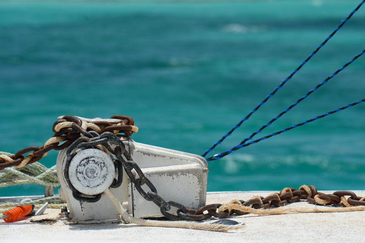 A close-up of a boat's anchor winch with tangled chains and ropes, set against turquoise ocean water.