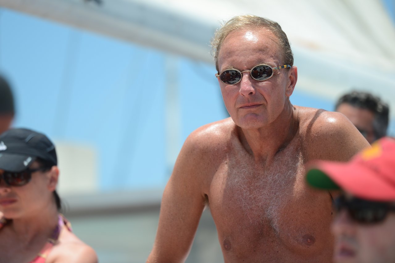 A shirtless man wearing sunglasses looks ahead while outdoors in Cancun, with other people around him.