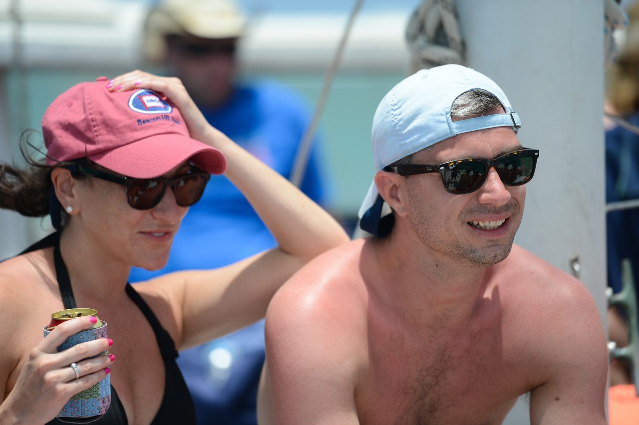 A man and woman wearing sunglasses and hats relax on a boat in sunny weather.