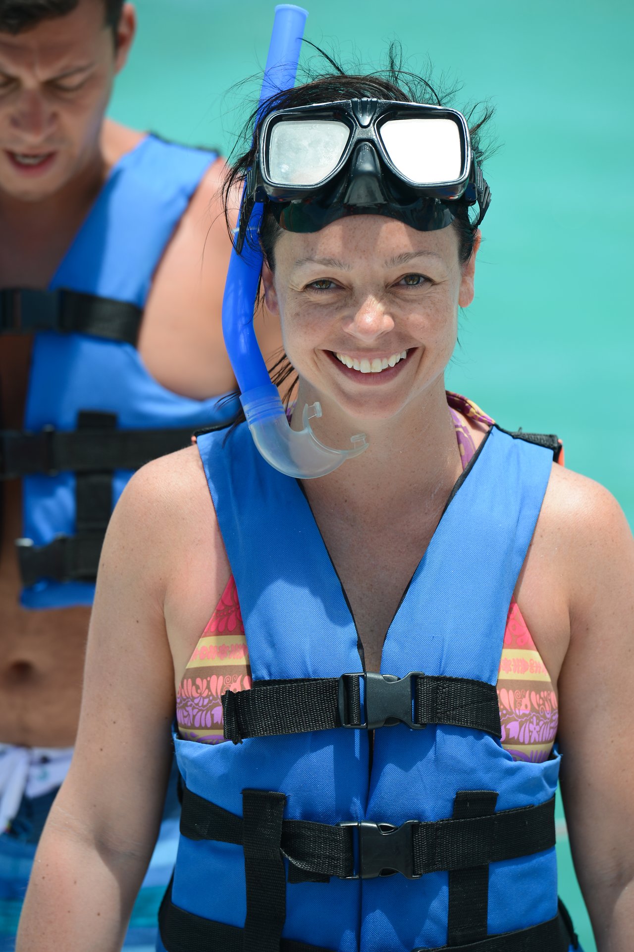 A smiling woman wearing a snorkel mask and life vest stands in clear water, ready for snorkeling.