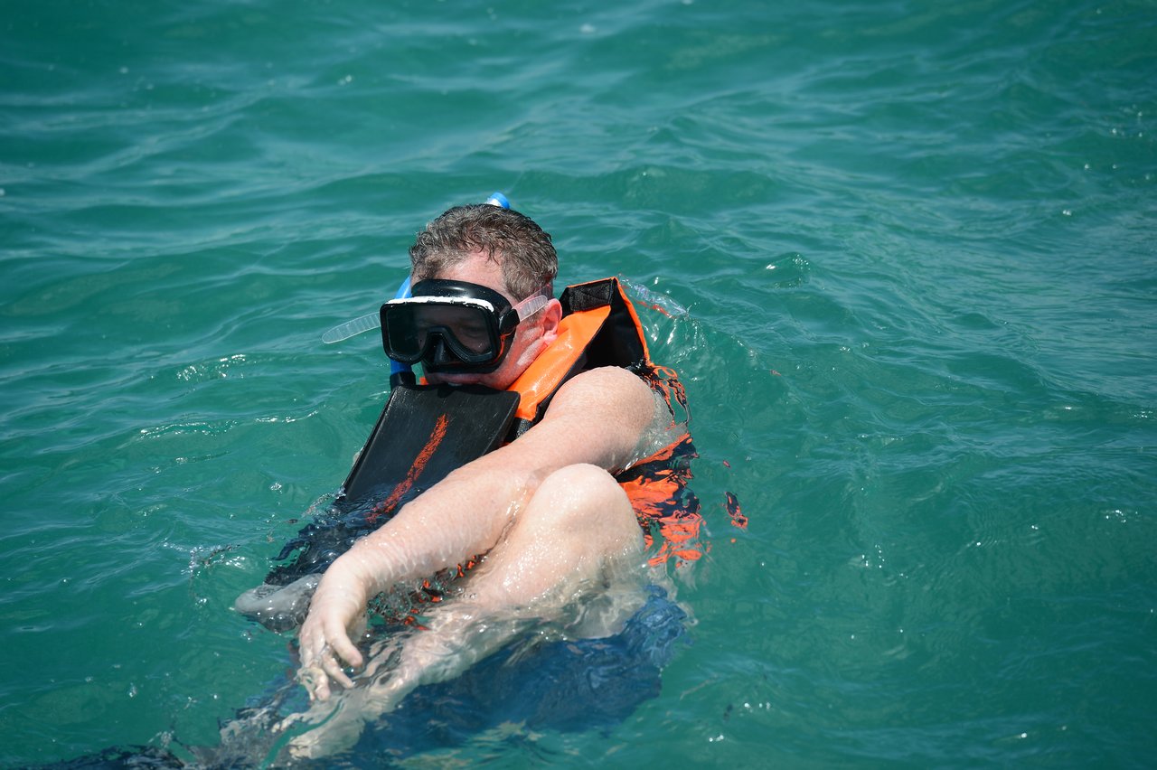 A person wearing a snorkel mask and life vest floats in the water, partially submerged.