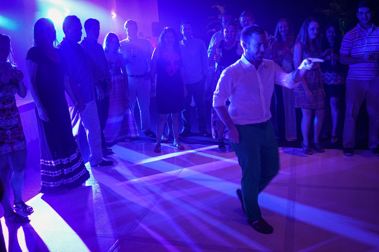 A man in a white shirt and green pants dances while a crowd watches at an award party.