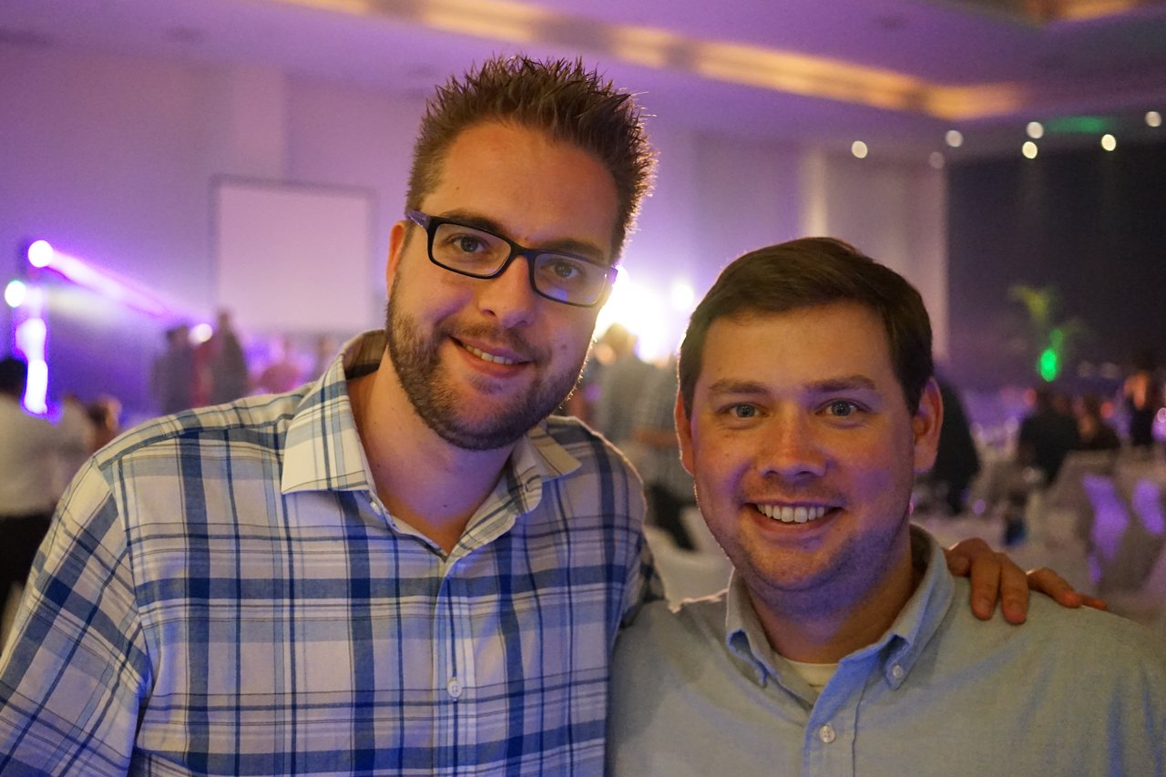 Two men smiling and posing together at an award party, with one placing his arm around the other.