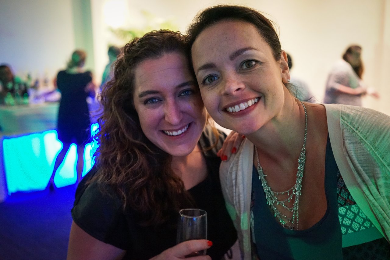 Two smiling women pose closely together at an award party, one holding a drink.