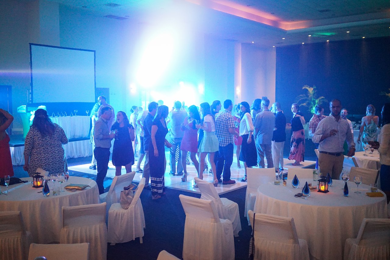 People are gathered in a decorated hall, socializing and dancing under bright lights at an award party.