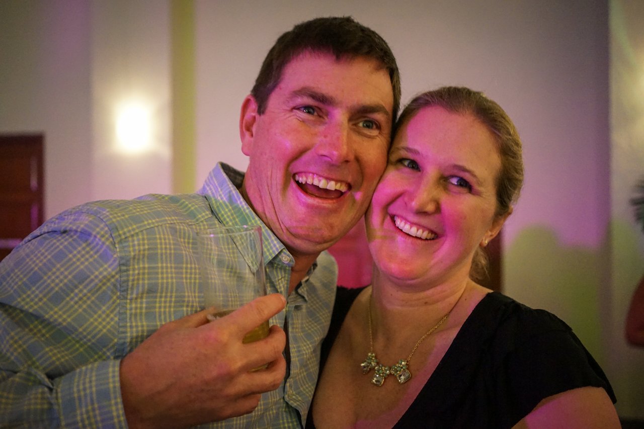 A smiling man and woman pose together at an award party, with the man holding a drink.