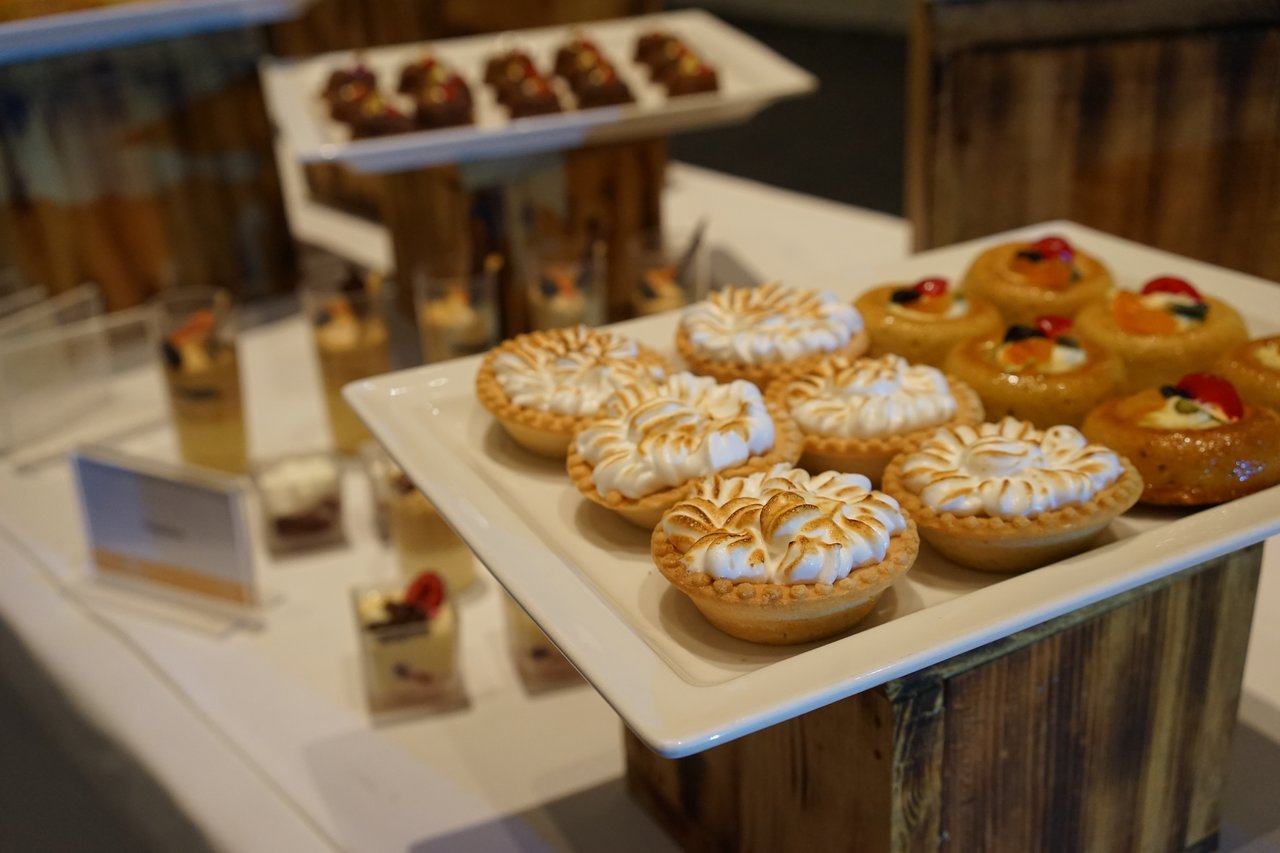 A table with assorted desserts, including meringue-topped tarts and fruit pastries, arranged on white plates at an event.