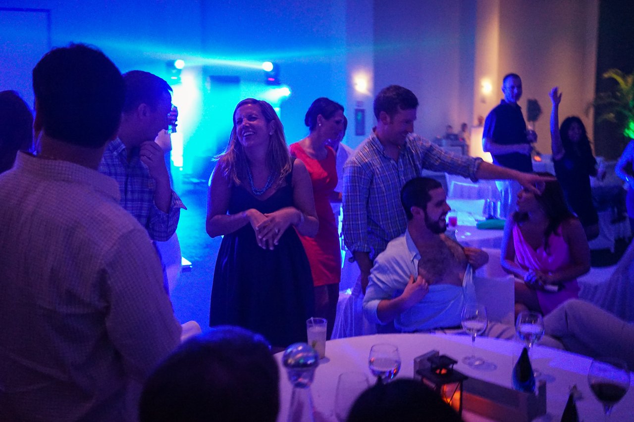 People laughing and talking at an award party, with one man playfully opening his shirt while others react.