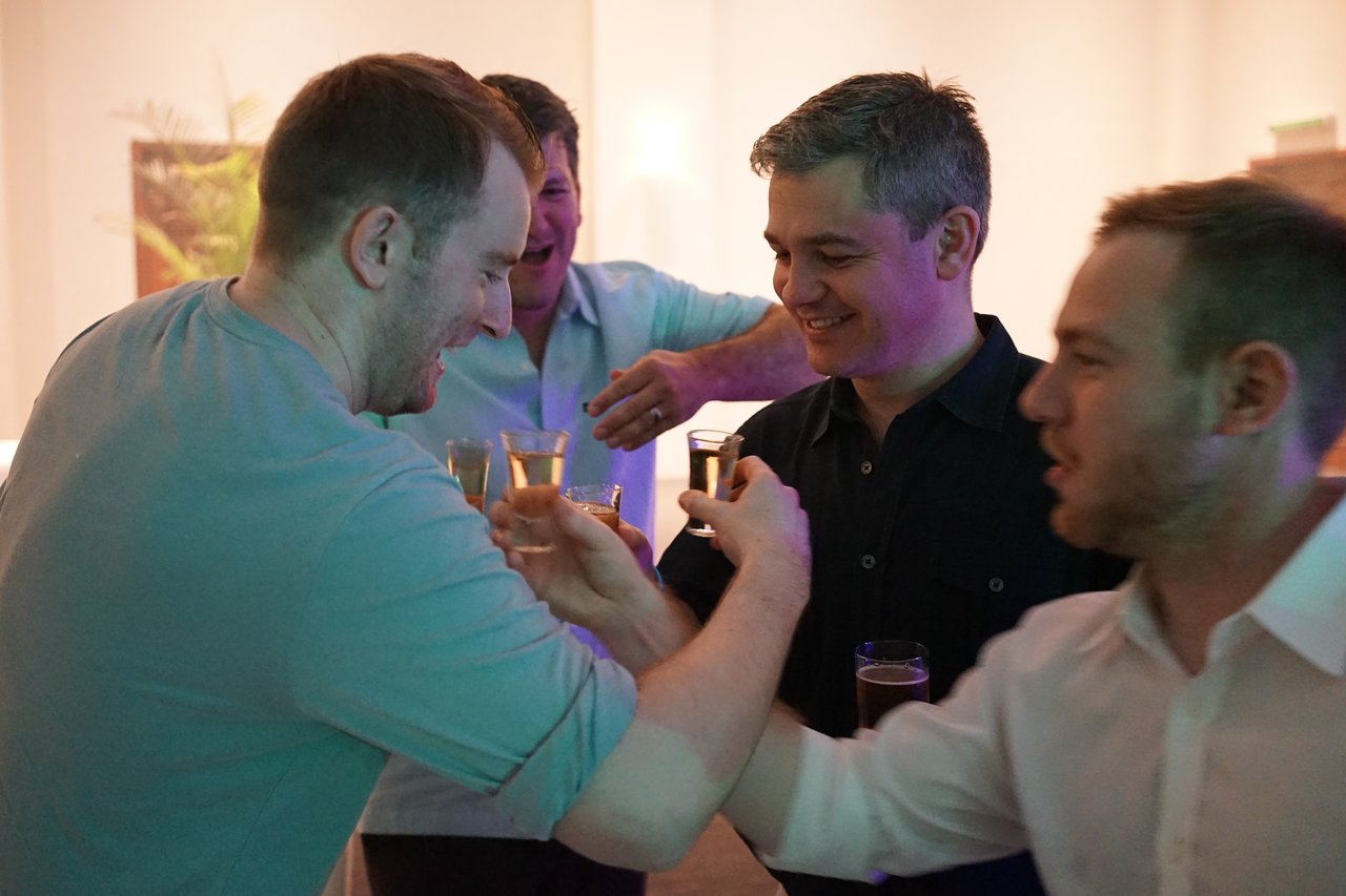 A group of men smiling and toasting with shot glasses at an award party.