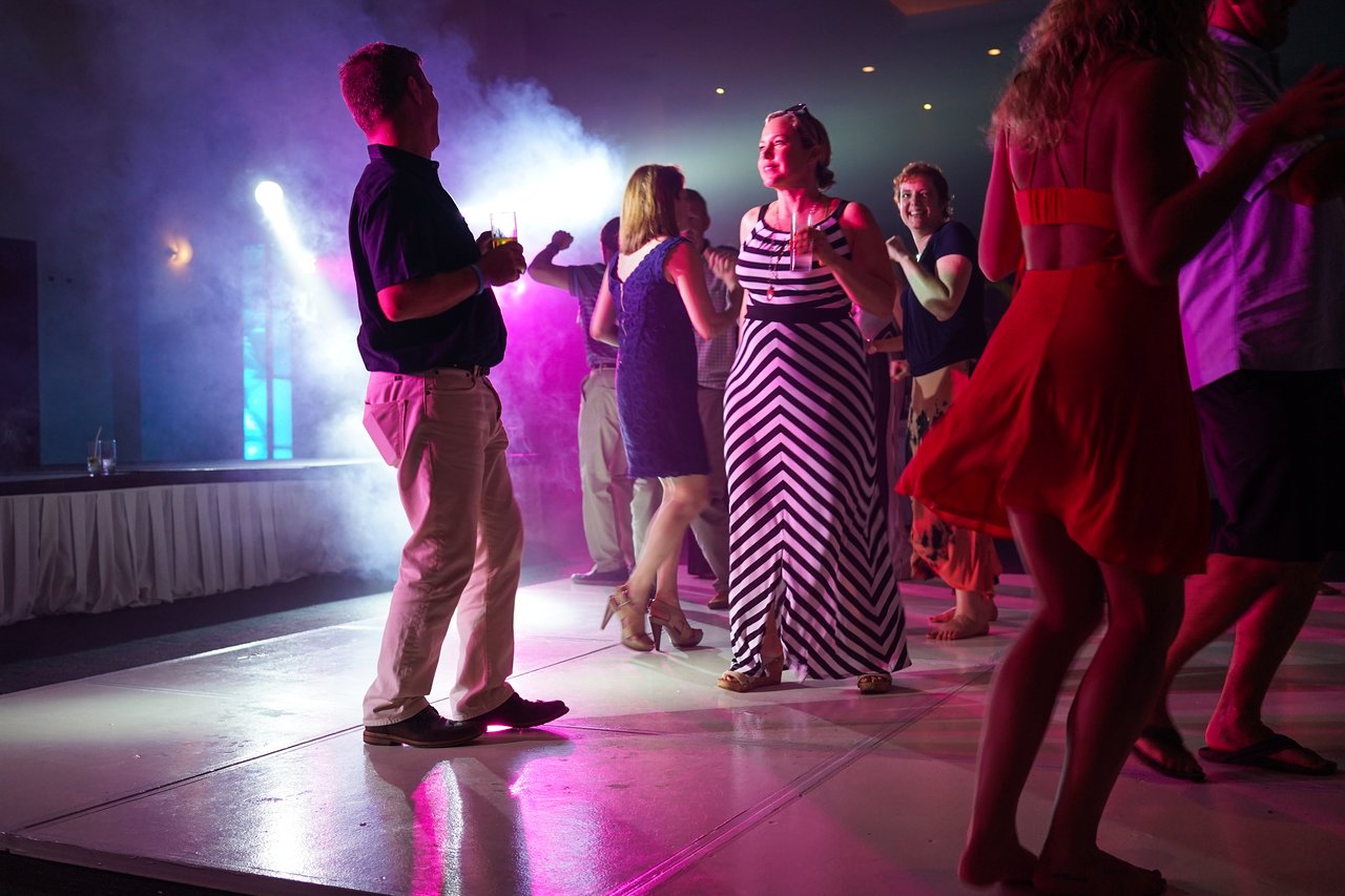 People dance under colorful lights at an award party, enjoying the celebration with drinks and lively movement.