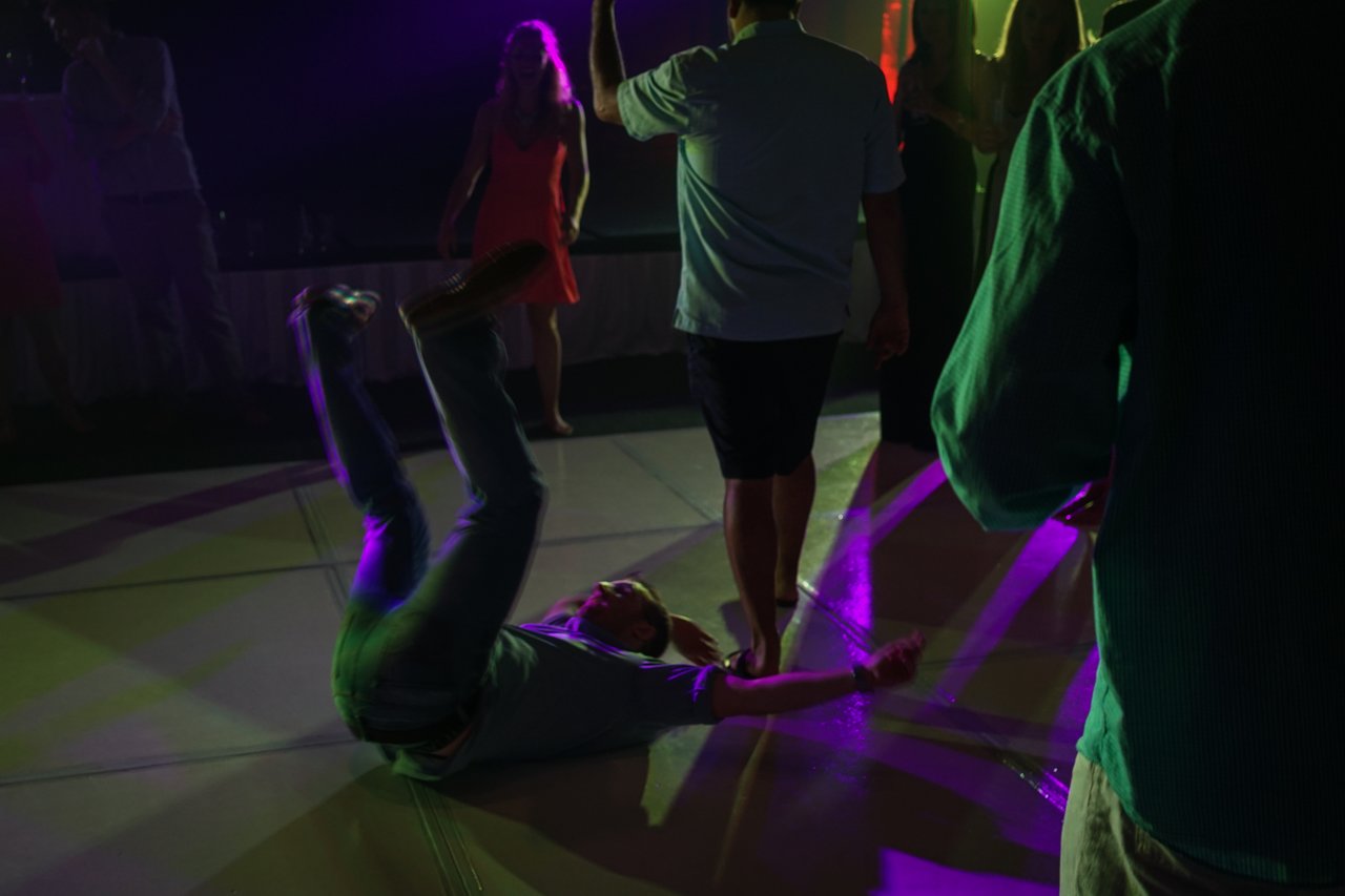 A man in a light-colored shirt and jeans is lying on the dance floor with his legs in the air.