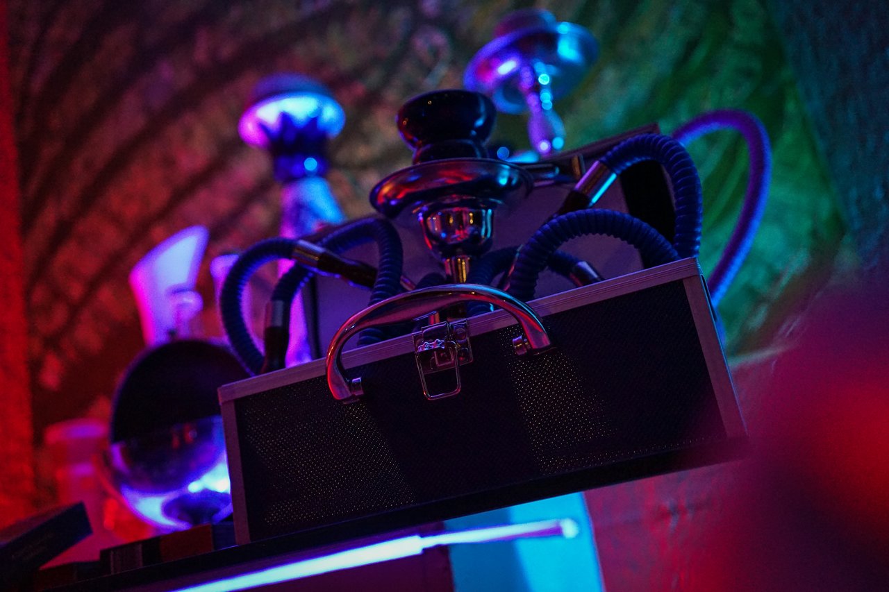 Hookahs with colorful hoses are displayed on a table under dim, colorful lighting at an award party.
