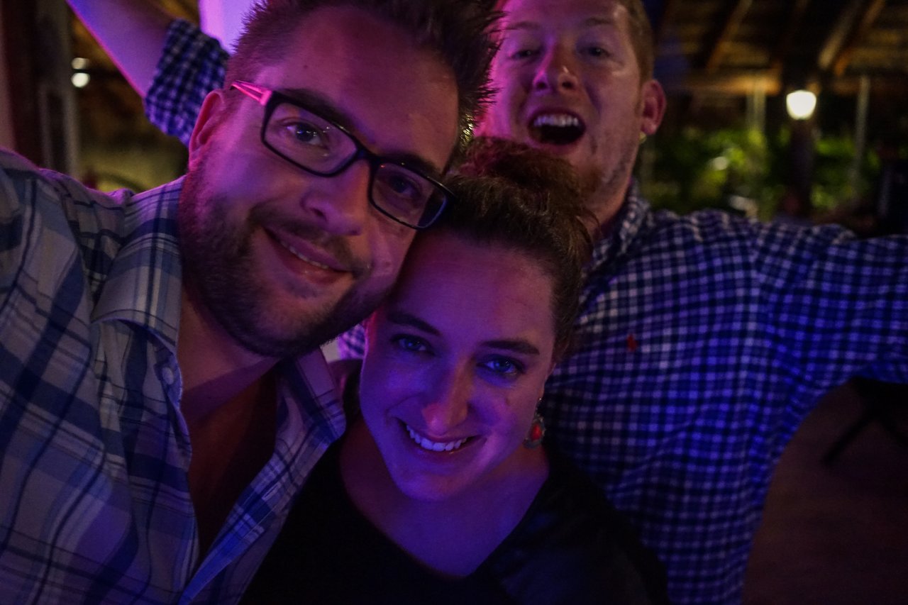 Three people smiling and posing closely together at an award party, with one person playfully in the background.