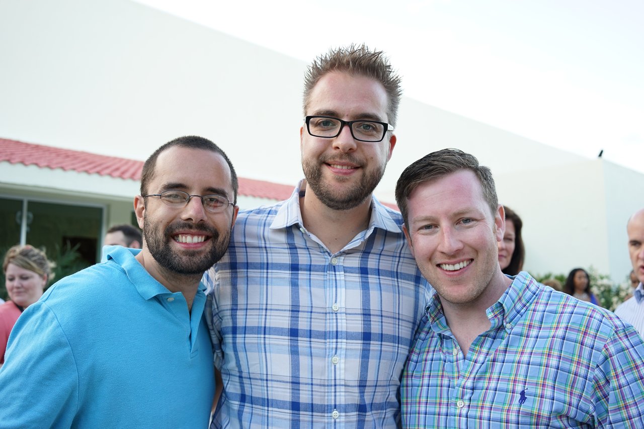 Three men in plaid and polo shirts smile and pose together at an outdoor award party.