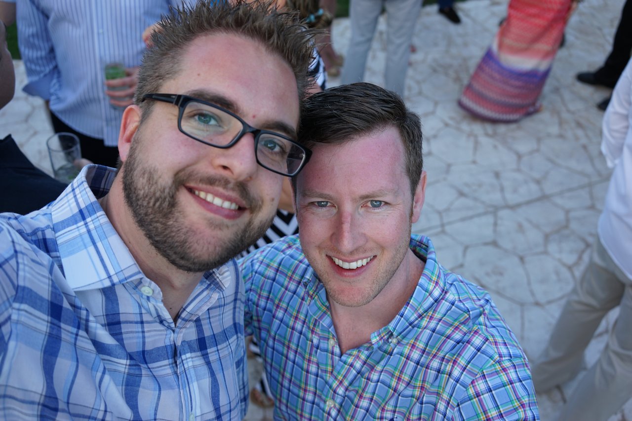 Two men in plaid shirts smile for a selfie at an outdoor award party with other guests in the background.