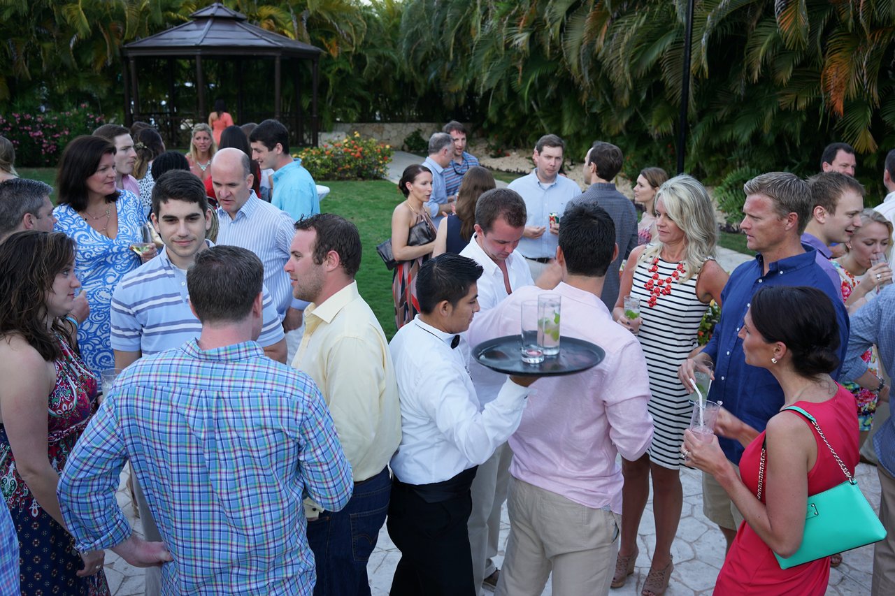 A waiter carries a tray with drinks while a large group of people socialize at an outdoor award party.
