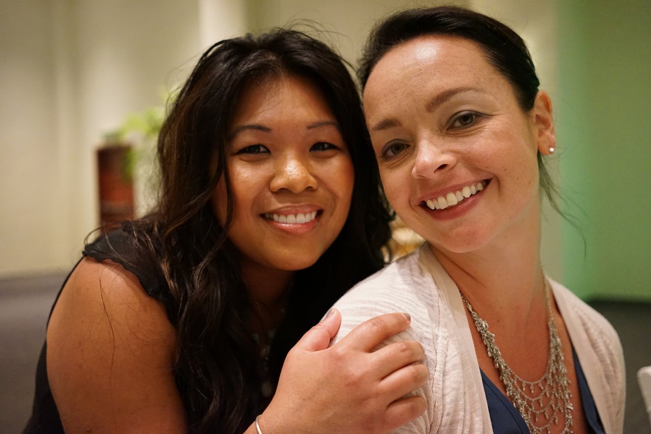 Two smiling women pose closely together at an award party, one resting her hand on the other's shoulder.