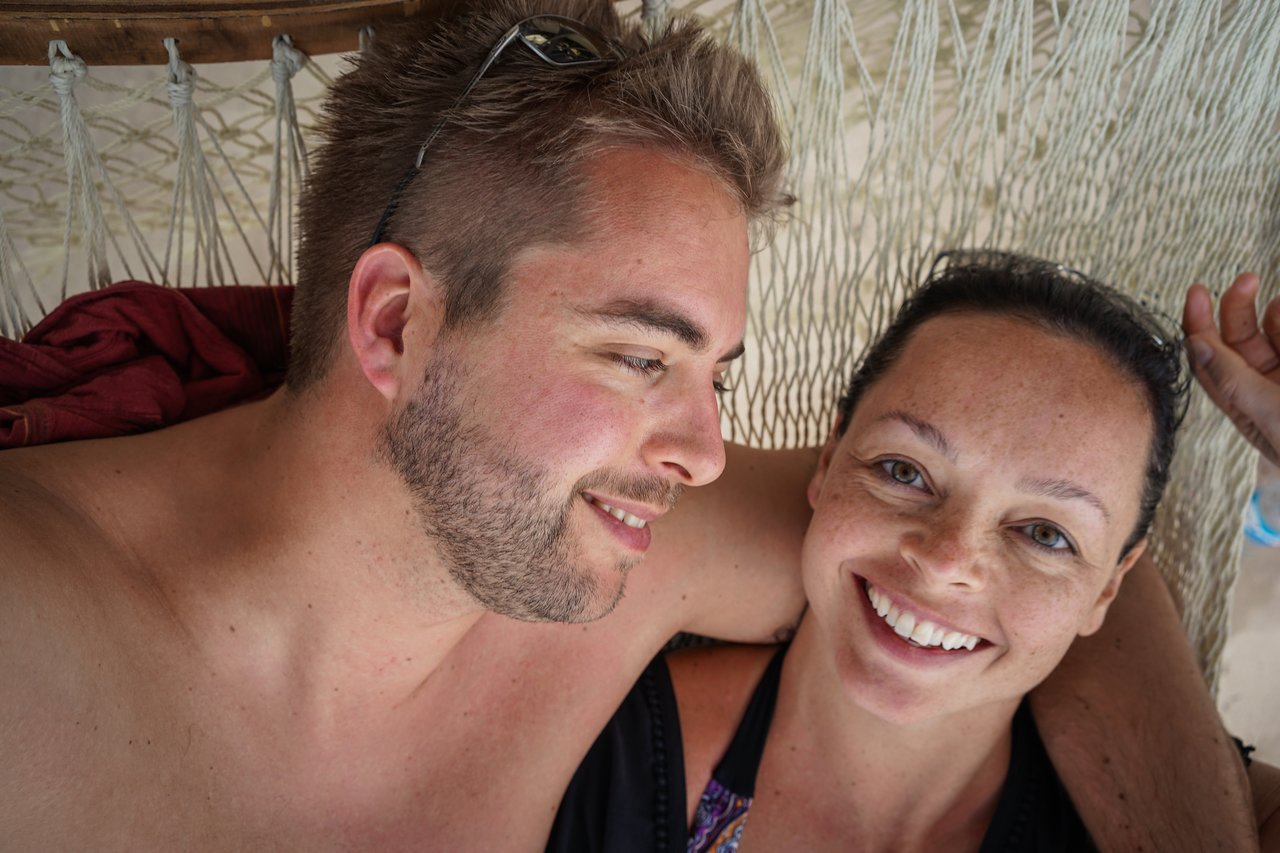 A smiling couple relaxes together in a hammock, looking at each other.
