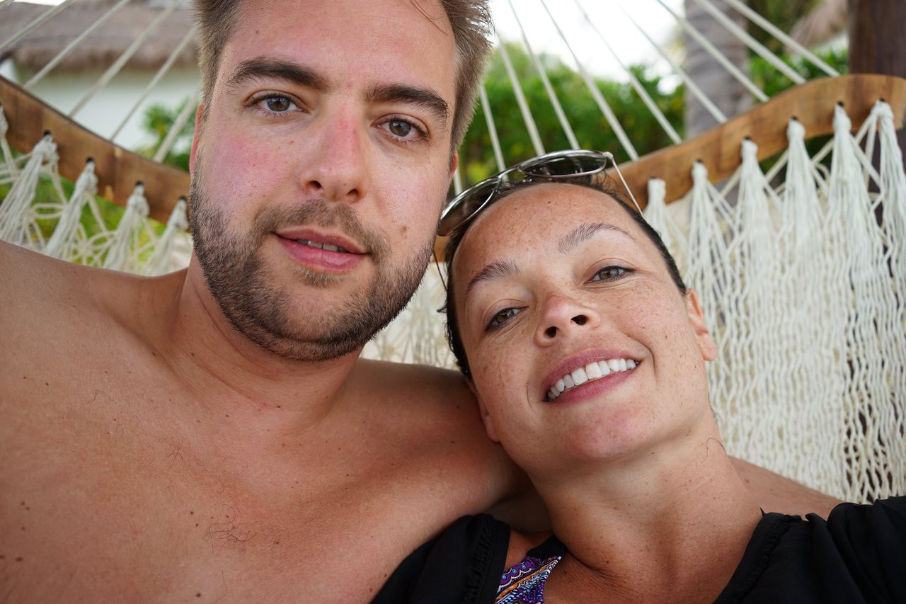 A man and woman relax together in a hammock, smiling at the camera.