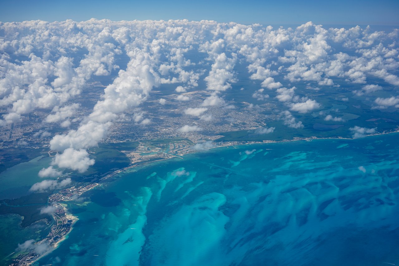 Aerial view of a coastal city in Mexico, with blue ocean waters and scattered white clouds above.