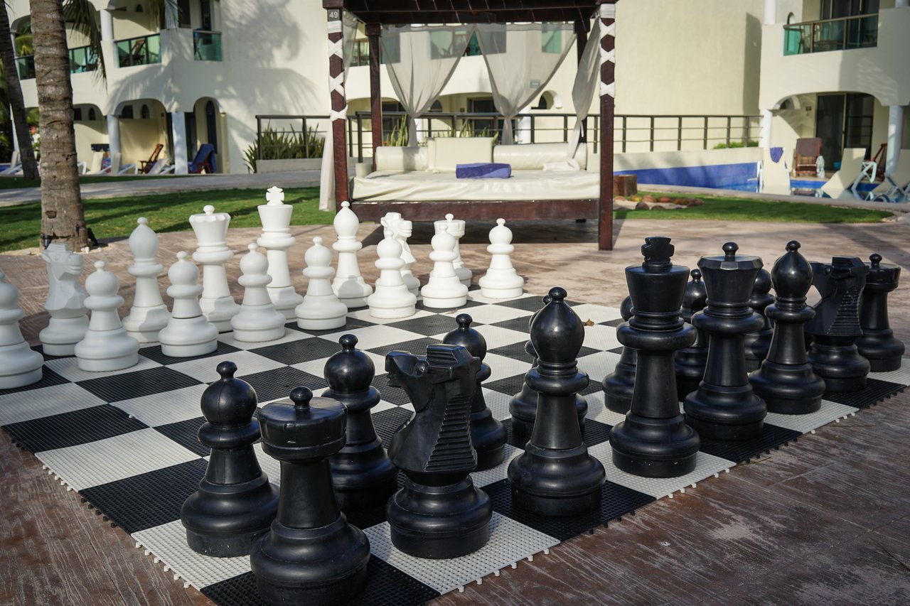Large outdoor chessboard with black and white pieces set up for a game on a patio.