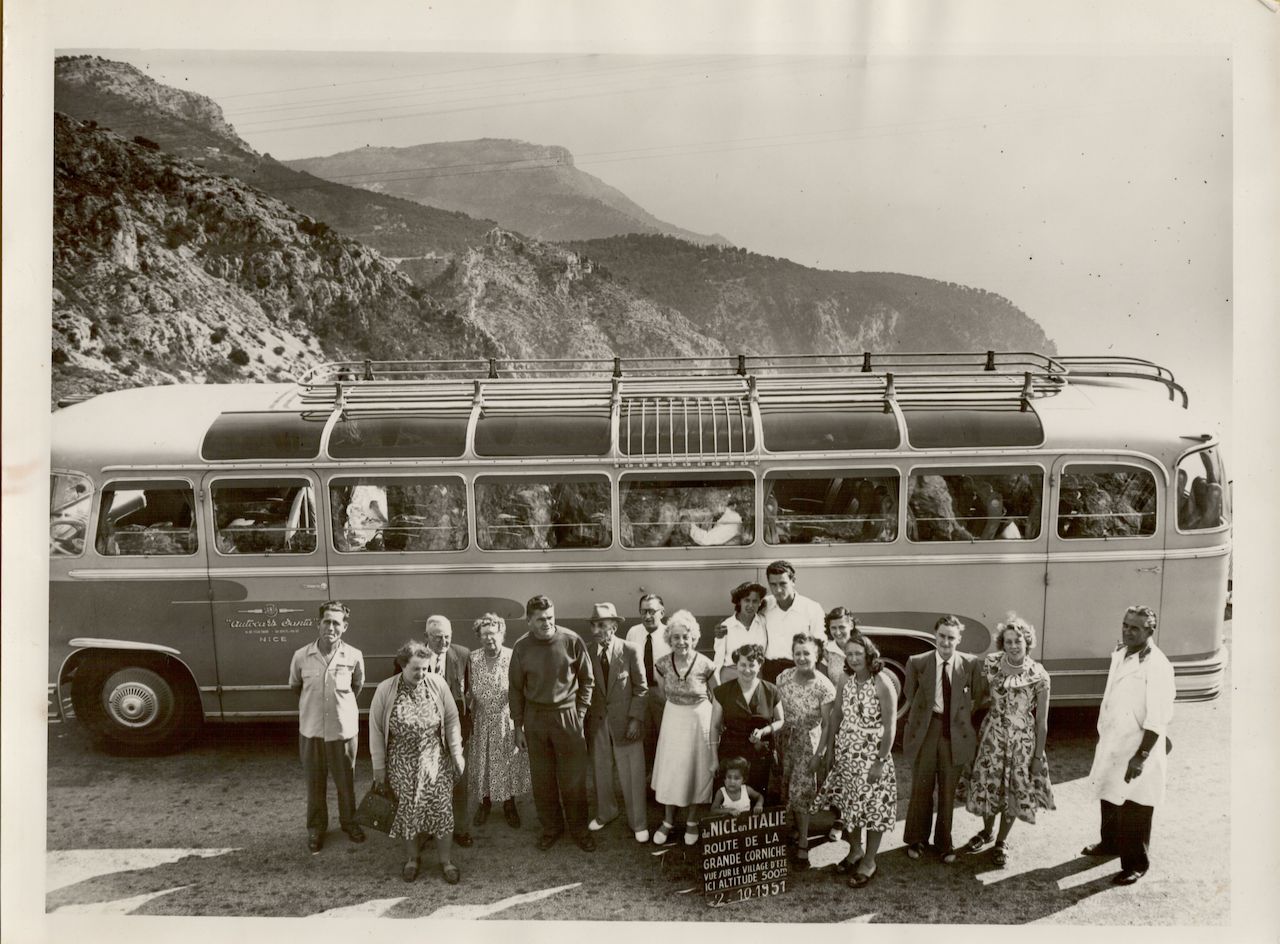 A group of people poses in front of a tour bus on a mountain road near Nice, France, in 1951.