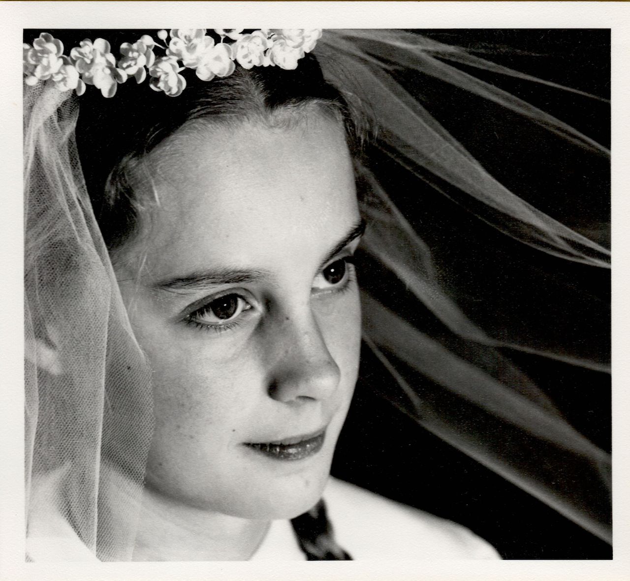 A young girl wearing a veil and floral headpiece looks to the side on her First Communion day.