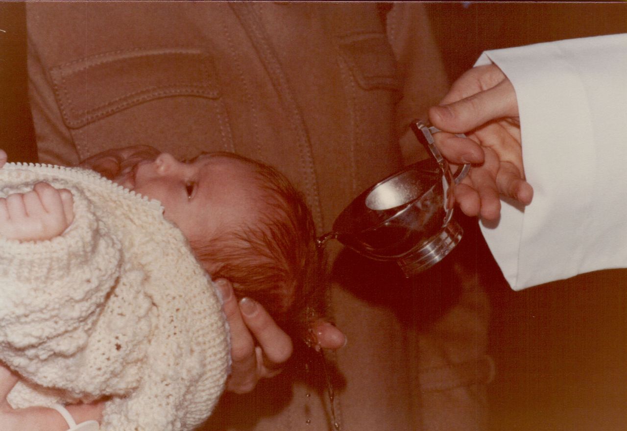 A baby is held while water is poured over their head during a baptism ceremony.