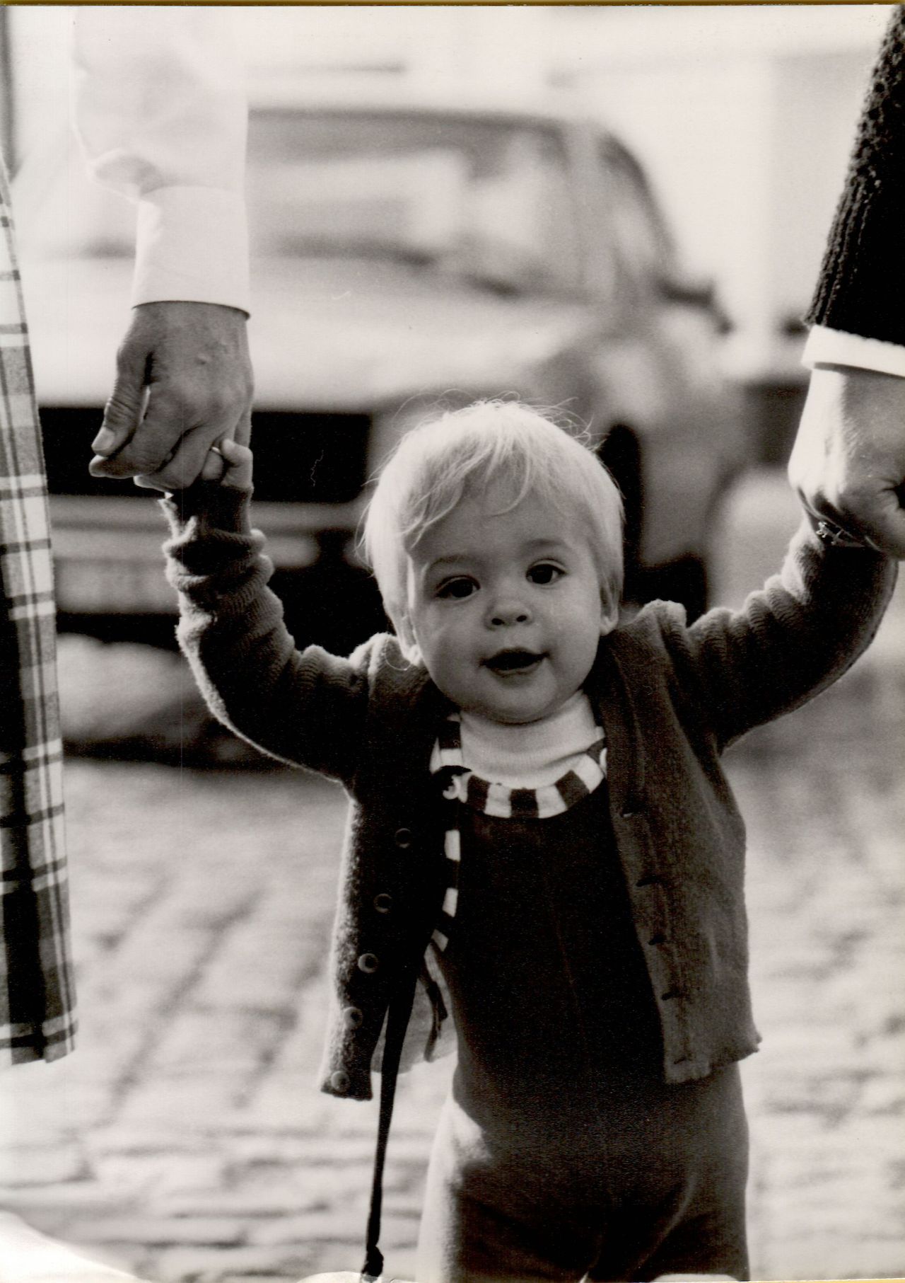 A young child walks while holding hands with two adults, looking forward with a happy expression.