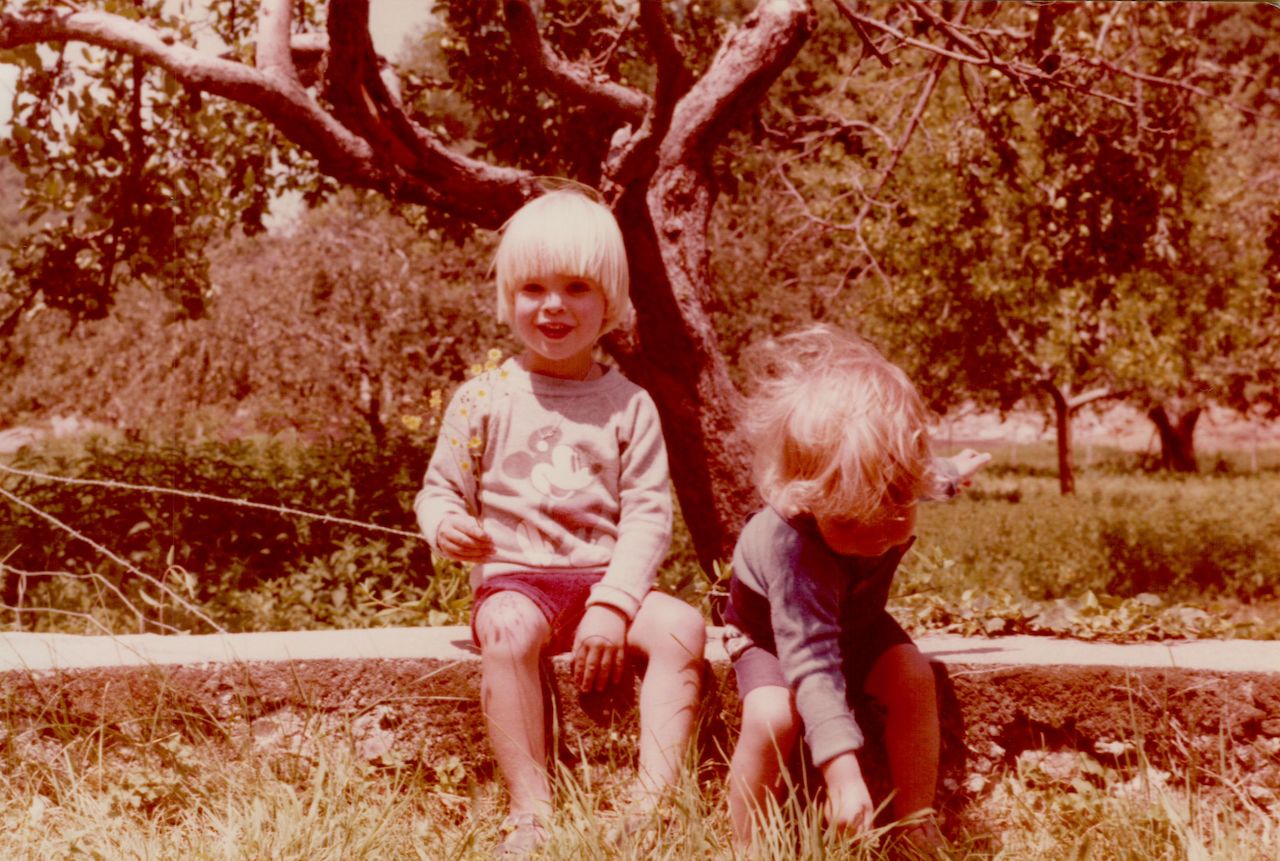 Two young children sit on a low wall outdoors.