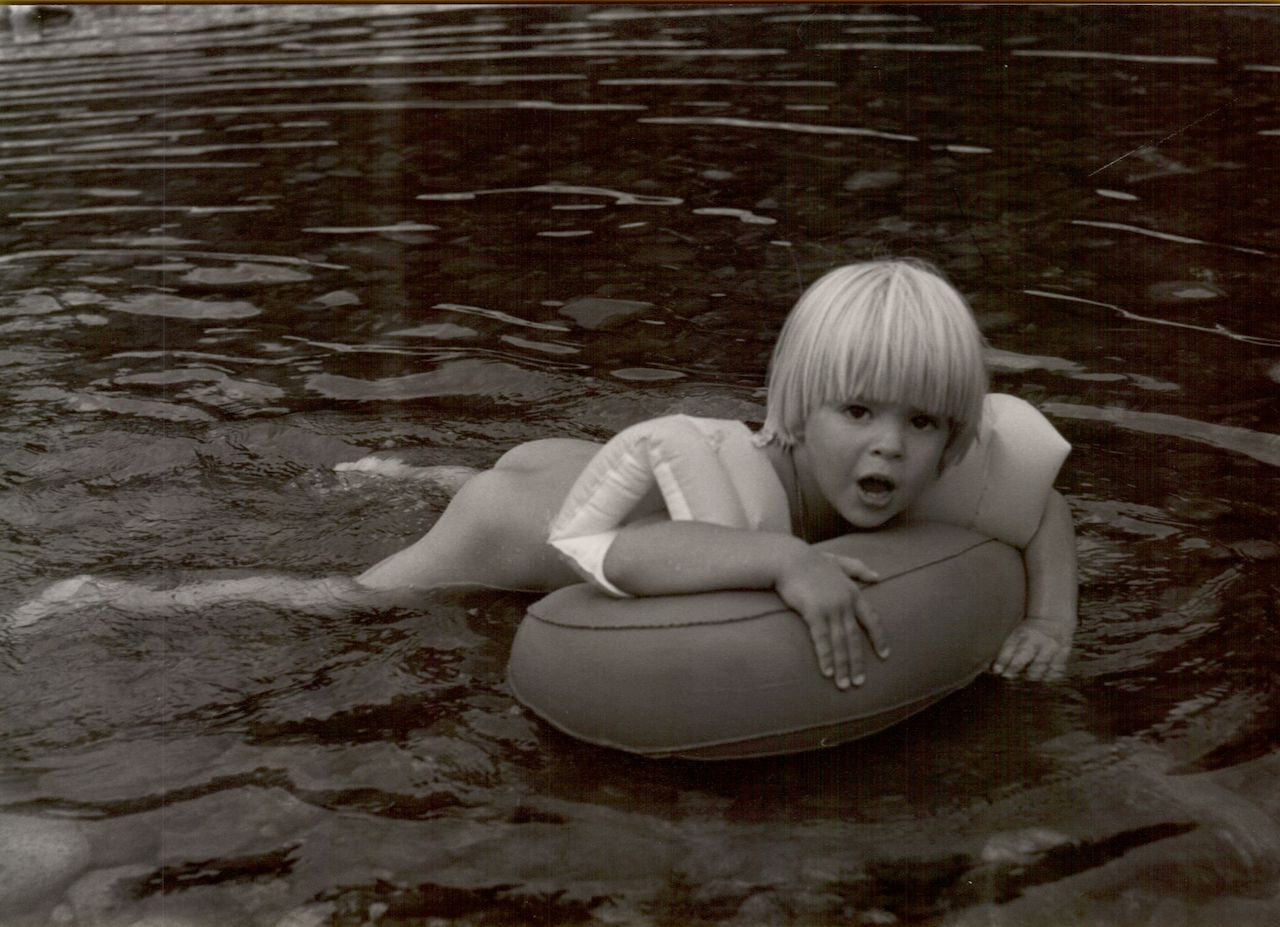 A young child with floaties leans on an inflatable ring while floating in the water.