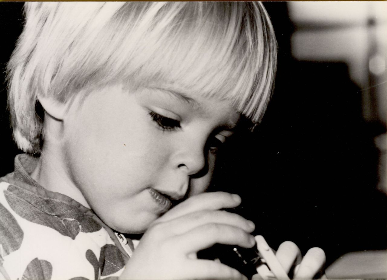 A young child with light hair carefully manipulates a small object with both hands, focusing intently.