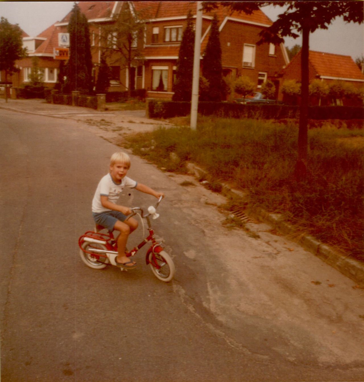 A young child rides a small red bicycle on a residential street, looking excited.