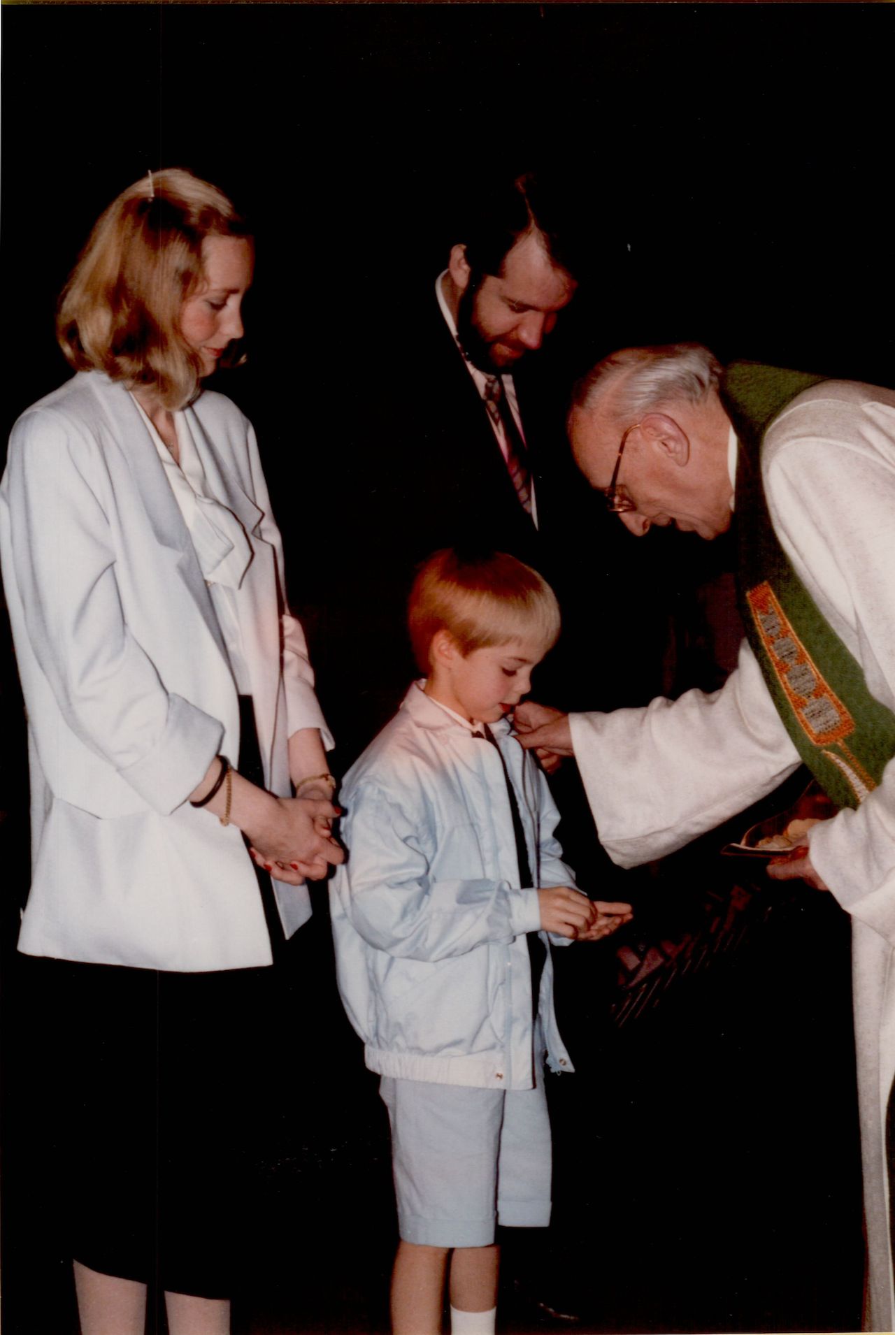 A priest gives communion to a young boy while two adults stand nearby, watching the ceremony.